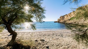 Ein Strand mit klarem, blauem Wasser, einem sandigen Ufer und felsigen Klippen.