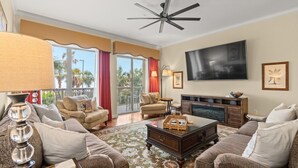 A spacious living room with a large flat-screen TV, comfortable seating, a fireplace, and a balcony with red curtains. - One-of-a-Kind 4 Bed / 4 Bath Oceanfront Retreat | ML03 (Myrtle Beach)