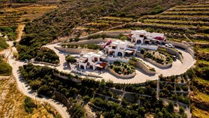 Una villa bianca con un viale curvo, circondata da giardini a terrazze e uno sfondo montuoso.