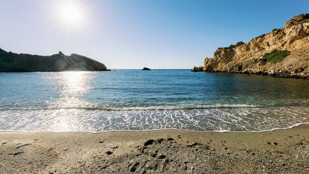 Una spiaggia con acque cristalline, scogliere rocciose e impronte sulla sabbia.