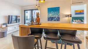 Ein modernes Wohnzimmer mit einem Holzes Esstisch, schwarzen Stühlen, einem Fernseher und Kunstwerken an den Wänden.
