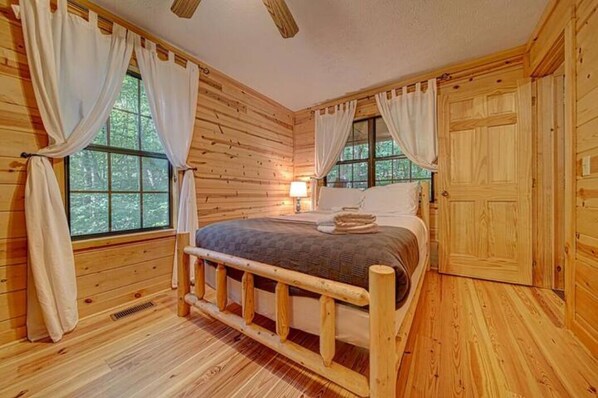 Camera da letto in una baita di legno, con un letto, tende, una finestra e un comodino.