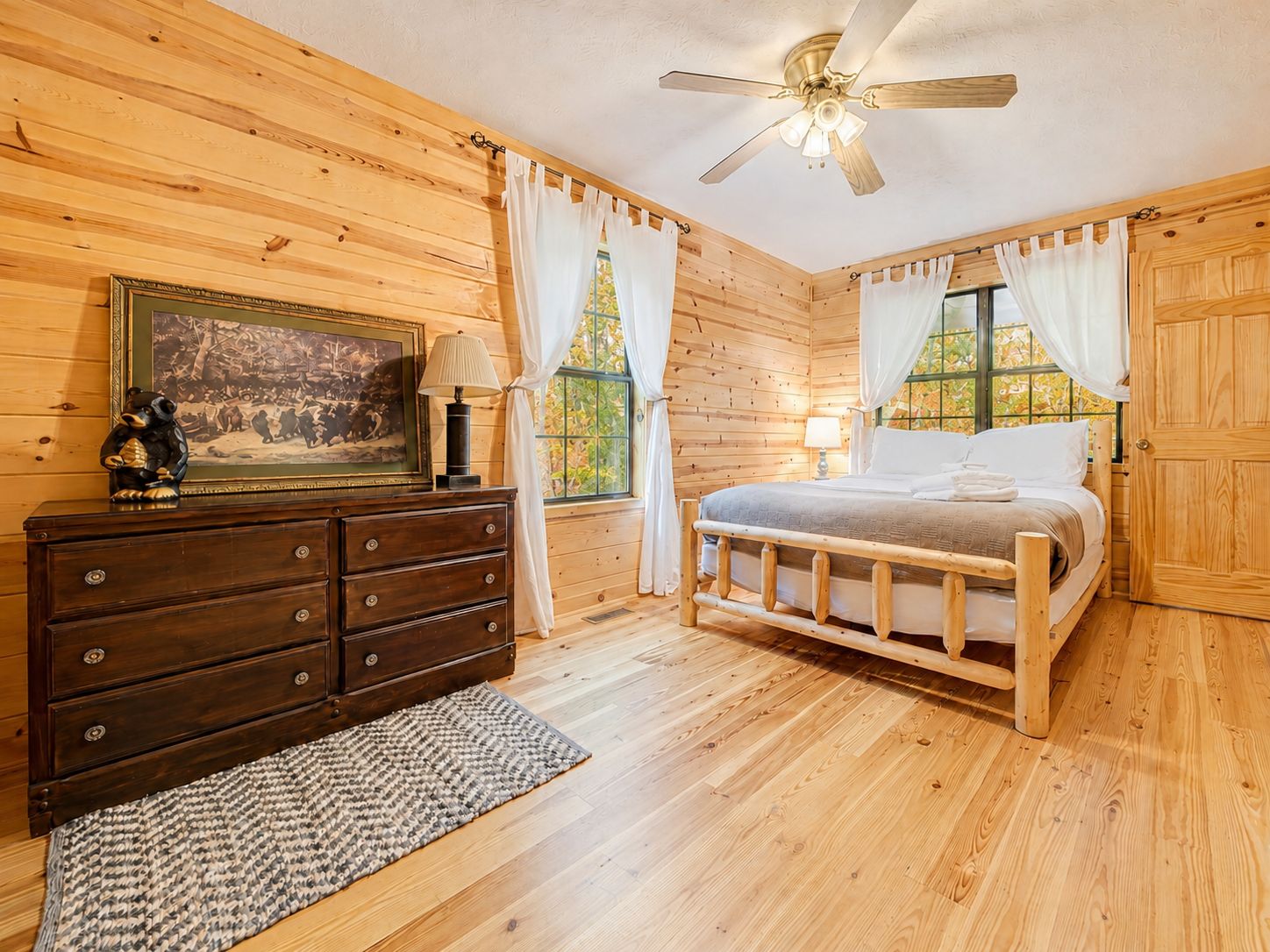 A wooden-paneled bedroom with a bed, dresser, and a ceiling fan.