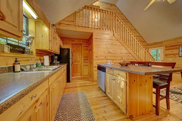 A wooden cabin interior with a kitchen, dining area, and a staircase leading to a loft. - Private 2BR Cabin Fireplace, Deck + Firepit (Blairsville)