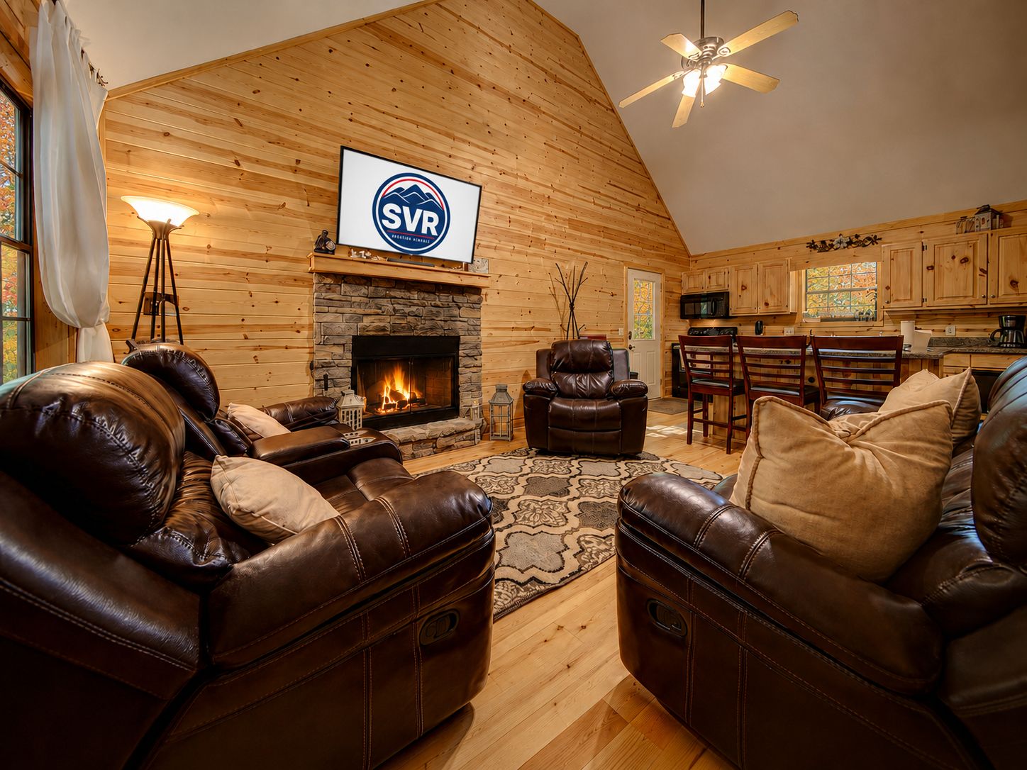 Interior acogedor de una cabaña con chimenea de piedra, mobiliario de cuero y un televisor montado que muestra 'SVR'.