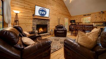 Interior acogedor de una cabaña con chimenea de piedra, mobiliario de cuero y un televisor montado que muestra 'SVR'.