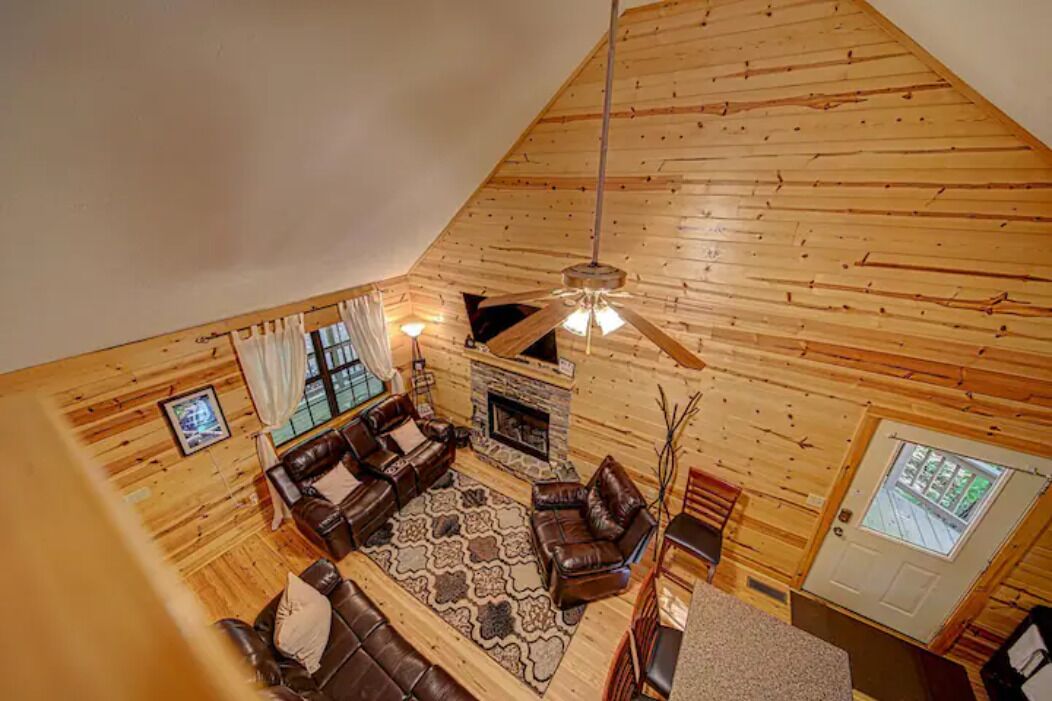 L’intérieur d’une cabane en rondins, avec une cheminée, des canapés en cuir et un plafond haut.