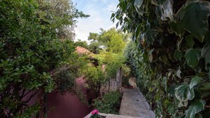 A narrow stone pathway leading to a building with a red-tiled roof, surrounded by lush greenery and flowering plants. - Nice Home in Postira With 5 Bedrooms, Wifi and Outdoor Swimming Pool (Postira)