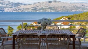 A wooden table with wicker chairs, a vase of white flowers, and a view of the sea and mountains. - Nice Home in Postira With 5 Bedrooms, Wifi and Outdoor Swimming Pool (Postira)