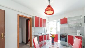 Una cocina moderna con armarios rojos y blancos, una mesa de comedor de vidrio y una lámpara colgante roja.