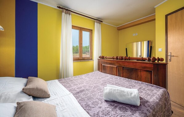 A hotel room with a bed, a wooden dresser, a mirror, and a window with curtains.