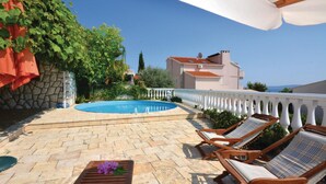 Area piscina con patio in pietra, sedie a sdraio e vista su un edificio sullo sfondo.