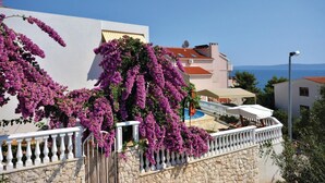 Un edificio costiero con parete in pietra, ringhiera del balcone bianca e tralci di bouganvillea viola.