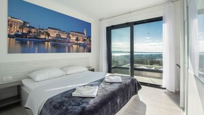 Una camera d'hotel moderna con un grande letto, un dipinto che raffigura uno skyline cittadino e un balcone con vista sulla città.