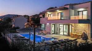 Una moderna casa a due piani con piscina, area relax esterna e vista sul paesaggio circostante.