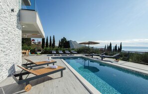 A pool area with lounge chairs, a wooden deck, and a view of the sea and mountains. - Nice Home in Kucine with WiFi, 4 Bedrooms & Hot Tub (Solin)