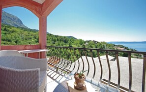 A balcony with wicker furniture, a potted plant, and a view of a mountainous landscape and sea.