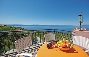 A balcony with a table set for two, a bowl of fruit, and a bottle of wine.