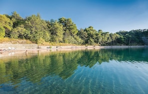 Un lago transparente con un muro de piedra y árboles a lo largo de la orilla.