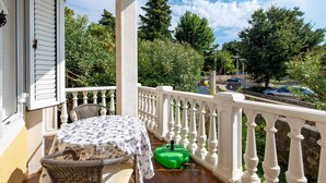 A balcony with a table and chairs, a green lawnmower, and a view of trees and a street. - Beautiful Apartment in Omisalj With 1 Bedrooms and Wifi (Omisalj)