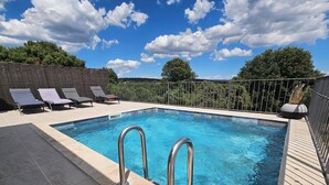 Una piscina rectangular con escaleras metálicas, rodeada de sillas de descanso y un solárium empedrado.
