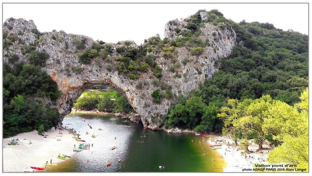 Un arco natural de roca sobre un río, con barcos y gente en la orilla.