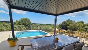 Un espacio al aire libre techado con piscina, mesa y sillas de madera.