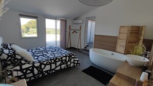 Un dormitorio moderno con una cama grande, una bañera y un baño con tocador de madera.