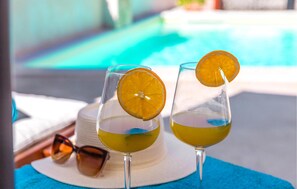 Two glasses of a yellowish beverage with orange slices, a white hat, and sunglasses on a blue surface near a pool. - Nice Home in Plovanija With Wifi and 3 Bedrooms (Buje)