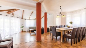 A spacious dining area with a wooden table and chairs, large windows with sheer curtains, and a high ceiling with exposed beams. - Beautiful Home in Pula With Wifi and 7 Bedrooms (Pula)