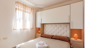 A neatly arranged bedroom with a bed, a window with sheer curtains, bedside lamps, and built-in storage cabinets. - Nice Home in Zminj with Hot Tub, WiFi & 1 Bedrooms (Zminj)