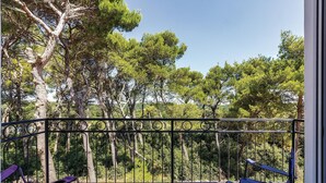 Un balcón con barandilla metálica, con vista a un área boscosa de árboles altos.