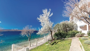 Blick auf die Küste mit blauem Meer, einem weißen Gebäude mit Balkon und einer grünen Parkanlage mit Bäumen.