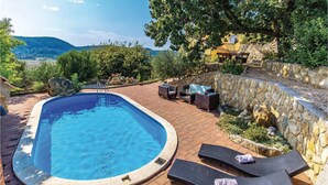 A swimming pool with lounge chairs and a stone wall, surrounded by greenery and a view of hills. - Nice Home in Supetarska Draga With Wifi and 3 Bedrooms (Rab)