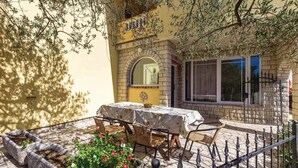 An outdoor patio with a table and chairs, surrounded by stone planters with flowers. - Nice Home in Supetarska Draga With Wifi and 3 Bedrooms (Rab)