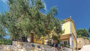 A stone-walled building with a yellow facade, a staircase leading to a balcony, and a large tree in front. - Nice Home in Supetarska Draga With Wifi and 3 Bedrooms (Rab)