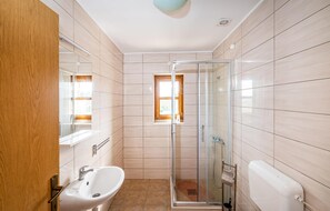 A bathroom with a glass shower enclosure, a sink, and a window.