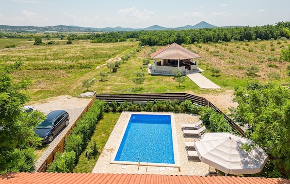 A villa with a swimming pool, outdoor seating, and a view of the surrounding landscape.