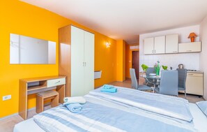 A hotel room with two beds, a desk, a wardrobe, a dining area with a table and chairs, and a kitchenette.