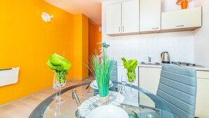 A modern kitchen with white cabinets, a glass dining table, and a bright orange wall. - Stunning Apartment in Stara Baska With Wifi (Punat)