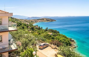 A coastal property with a car parked in the driveway, surrounded by lush greenery and a clear view of the sea.