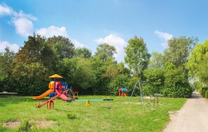 Explore a serene park with play structures for kids, surrounded by lush greenery and trees, and a paved path for easy access.