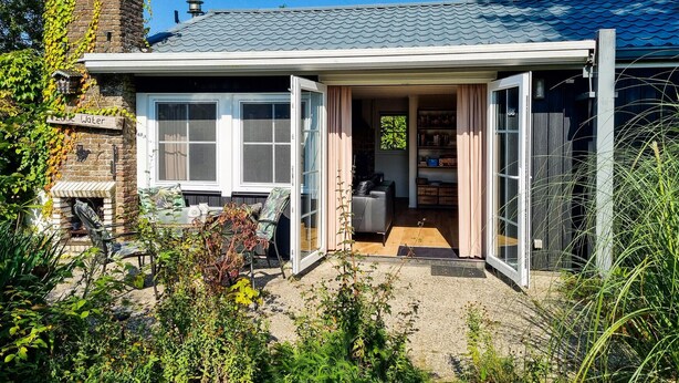 Una casa amb jardí, un patio amb mobles d'exterior i un interior visible que inclou una cuina i una sala d'estar.