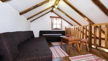 A cozy attic room with a dark sofa, a wooden table with a red bowl, and a window with curtains.