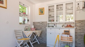 A kitchen with white cabinets, a dining table with chairs, and a window with a hanging plant. - Stunning Apartment in Dugi Rat With 2 Bedrooms and Wifi (Dugi Rat)