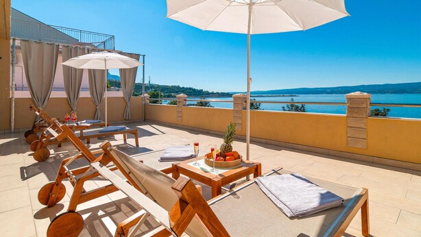 A sunlit outdoor seating area with wooden loungers, a table with a pineapple and drinks, and a view of a lake and mountains. - Stunning Apartment in Dugi Rat With 2 Bedrooms and Wifi (Dugi Rat)