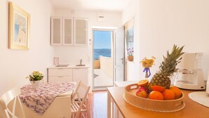 A kitchen with a view of the sea, a dining area with a table set for two, and a fruit bowl on the counter. - Stunning Apartment in Dugi Rat With 2 Bedrooms and Wifi (Dugi Rat)