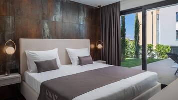 A modern hotel room with a large bed, two bedside tables, a large window with a view of the outside, and a dark wooden accent wall.