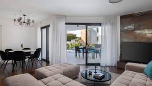 A modern living room with a sofa set, a dining table with chairs, a glass coffee table, and a view of an outdoor pool area through a glass door. - Amazing Home in Zidarici With Outdoor Swimming Pool, Wifi and 4 Bedrooms (Malinska-Dubasnica)