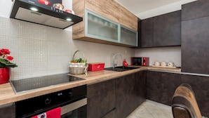 A modern kitchen with dark cabinets, a wooden countertop, a built-in microwave, and a red kettle on the shelf.